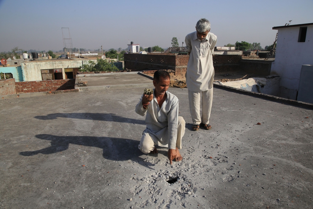 An Indian displays mortar shrapnel and points to a mortar impact point on the roof of a house following following cross-border firing between India and Pakistan, in Arnia sector about 35 km from Jammu, Wednesday. — AFP