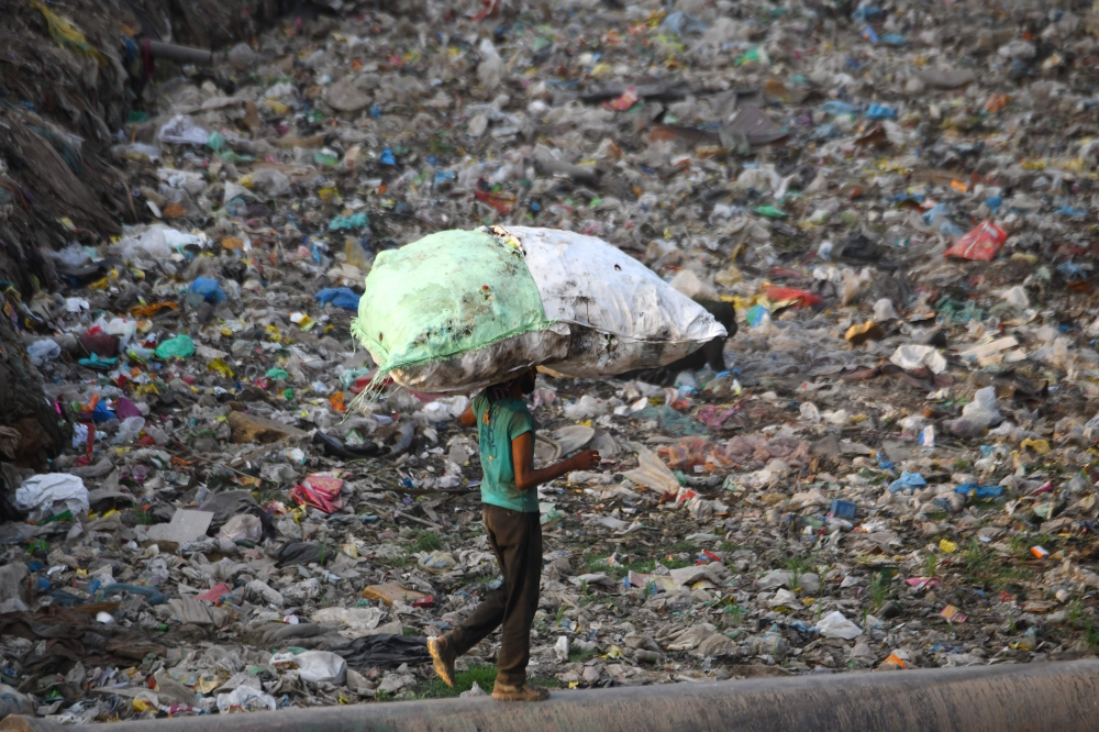 A man carries a bag containing plastic recyclable items as he walks on a water pipe next to a sewage drain canal full of garbage in the Taimur Nagar slum area in New Delhi in this May 30, 2018 file photo. — AFP