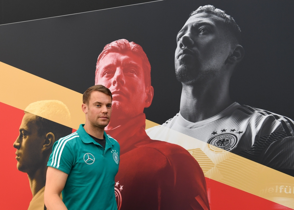 Germany's national football goalkeeper Manuel Neuer leaves a press conference in front of a poster featuring Germany's defender Joshua Kimmich (L), midfielder Toni Kroos (C) and defender Jerome Boateng (R) at the Rungghof training center on Monday in Girlan, near Bolzano, northern Italy, ahead of the FIFA World Cup 2018 in Russia. — AFP