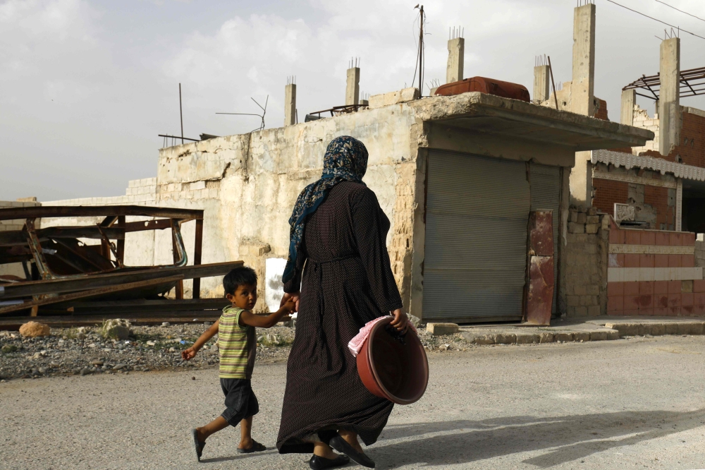 A Syrian woman walks past destroyed buildings in Kobane. — AFP