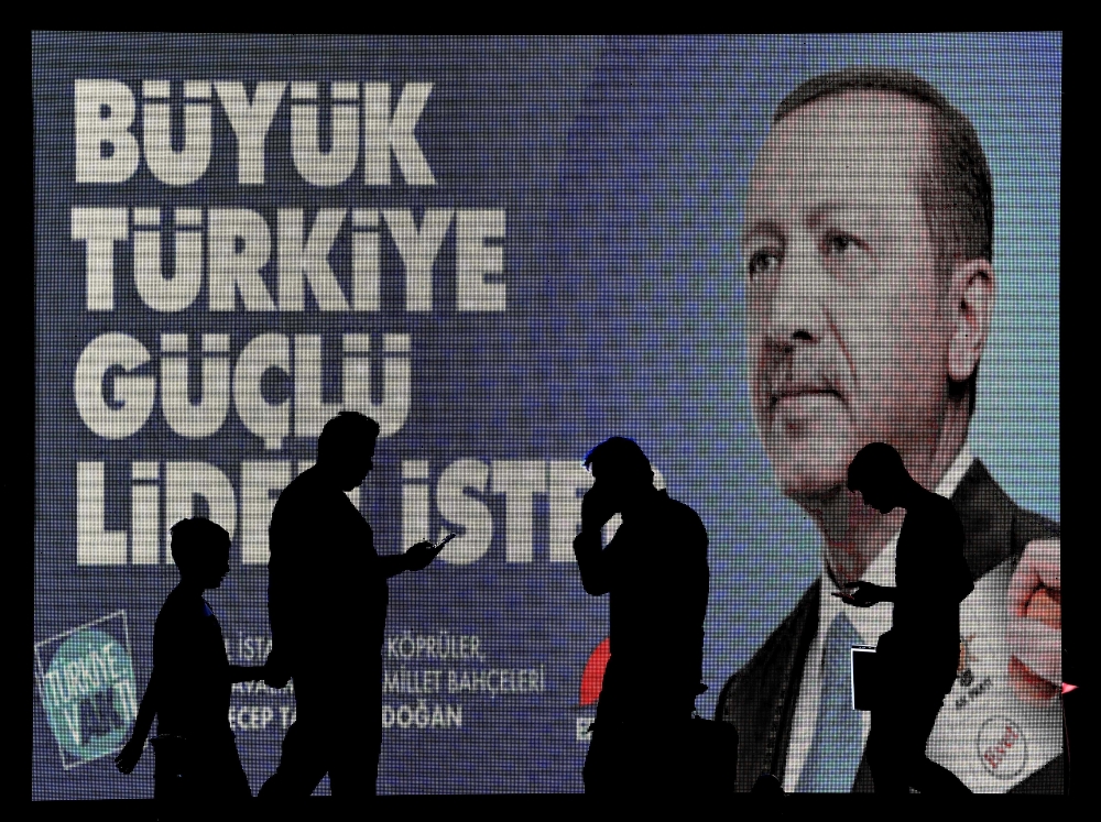 People are pictured in silhouette against campaign banners with the portrait of Turkey's President in Istanbul. Turkey prepares for tight presidential and parliamentary elections on June 24, while many analysts say President Recep Tayyip Erdogan wants a major foreign policy success to give him a final boost. The slogan reads 
