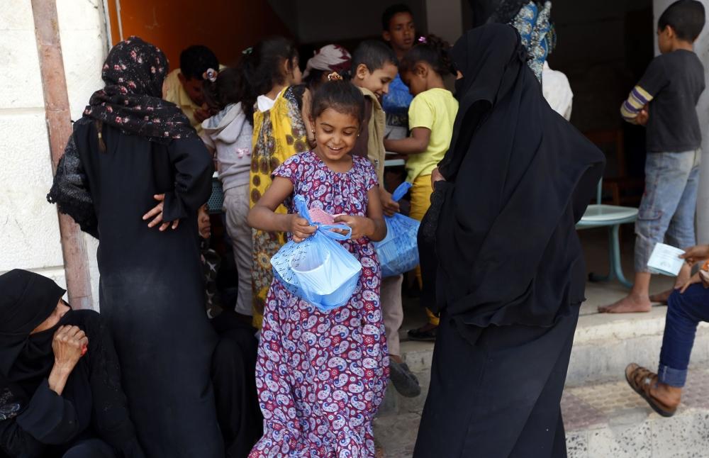 A displaced Yemeni girl who fled home in the war-torn city of Hodeidah, smiles as she receives food provided by a charity in the capital Sanaa, Monday. — AFP