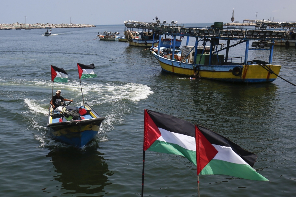 Palestinian fishermen seen on their boats with national flags at the seaport of Gaza City on Tuesday, while the fishing zone enforced by Israel off the Gaza Strip was also reduced from six nautical miles to three. — AFP