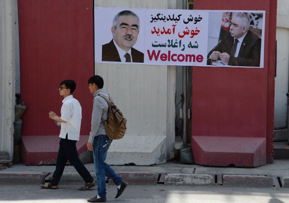 Afghan residents walk past a banner with the image of self-exiled Vice President Abdul Rashid Dostum ahead of his arrival to Kabul, Sunday. — AFP