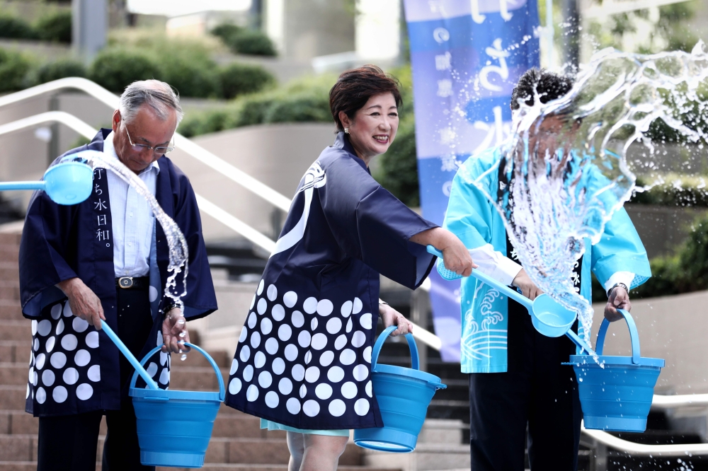 Tokyo Governor Yuriko Koike splashes water on the ground during a water sprinkling event called Uchimizu which is meant to cool down the area, in Tokyo on Monday. — AFP