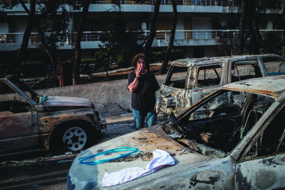 A woman with a cast stands among cars burned following a wildfire at the village of Mati, near Athens, on Tuesday. — AFP