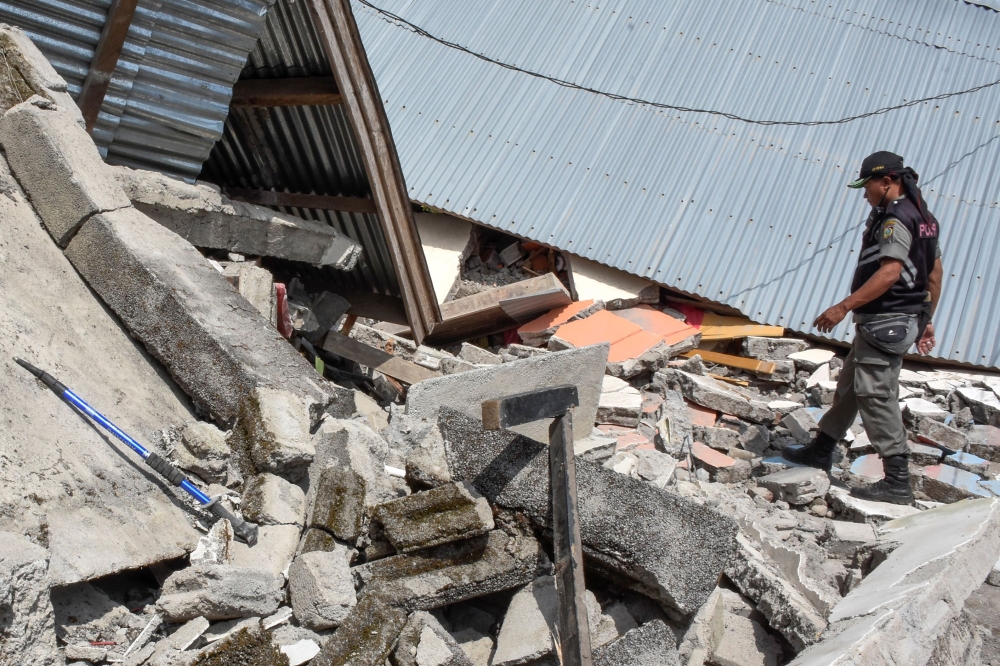 An Indonesian village security officer examines the debris of houses, after a 6.4 magnitude earthquake struck, in Lombok, on Sunday. — AFP
