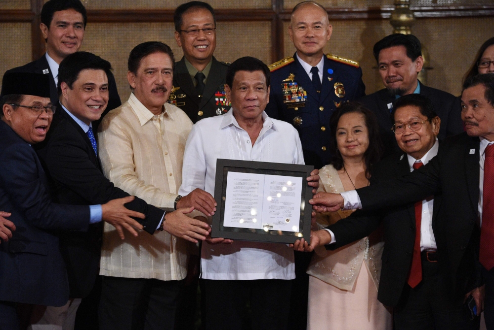 Philippine President Rodrigo Duterte (C) poses for photos along with Moro Islamic Liberation Front (MILF) chairman Murad Ebrahim (L), Senate President Vicente Sotto (3rd L), former president and now speaker of the house Gloria Arroyo (3rd R), Moro Islamic Liberation Front members Ghadzali Jaafar (2nd R) and Mohagher Iqbal (R) during the presentation ceremony of the signed document on the Organic Law for Bangsamoro Autonomous Region of Muslim Mindanao to the Moro Islamic Liberation Front (MILF) at Malacanang palace in Manila on Monday. — AFP