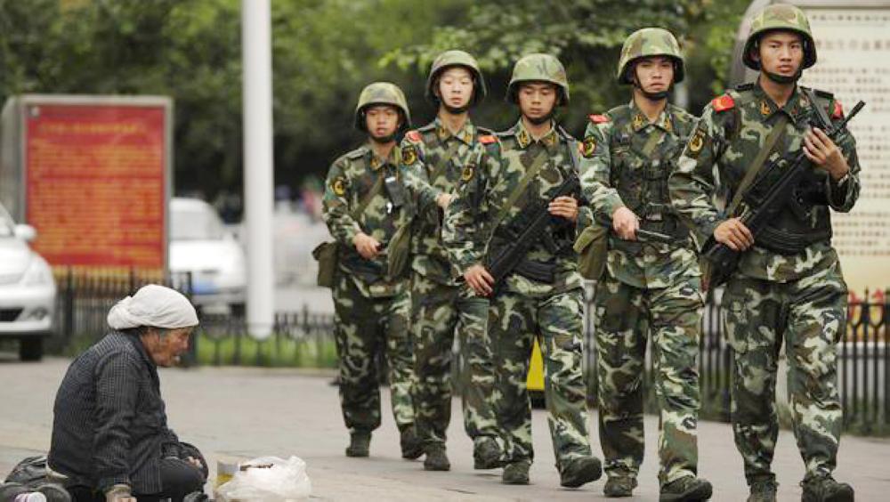 A Muslim Uighur woman begs as armed Chinese paramilitary police march past on a street in Urumqi, the capital of the Xinjiang region, in this July 5, 2010 file photo. — AFP