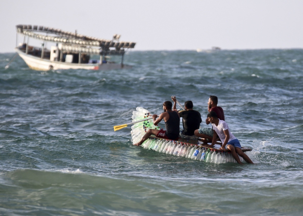 Palestinian fisherman Mouad Abu Zeid and his friends ride on his boat that he made of 700 empty plastic bottles in the sea in Rafah in the southern Gaza Strip on Tuesday. — AFP