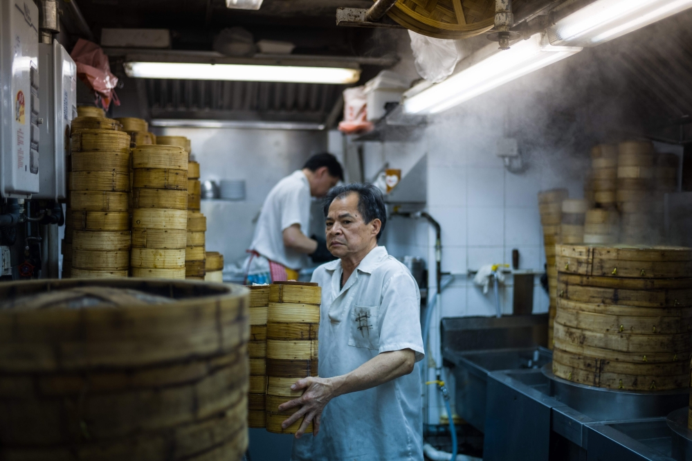 A kitchen worker carries bamboo dim sum steamers in the kitchen of the Lin Heung Tea House in Hong Kong. - AFP