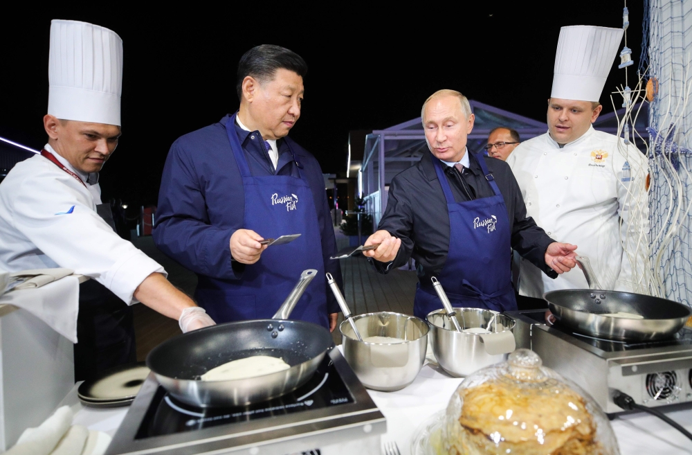 Russian President Vladimir Putin and his Chinese counterpart Xi Jinping cook pancakes while visiting 