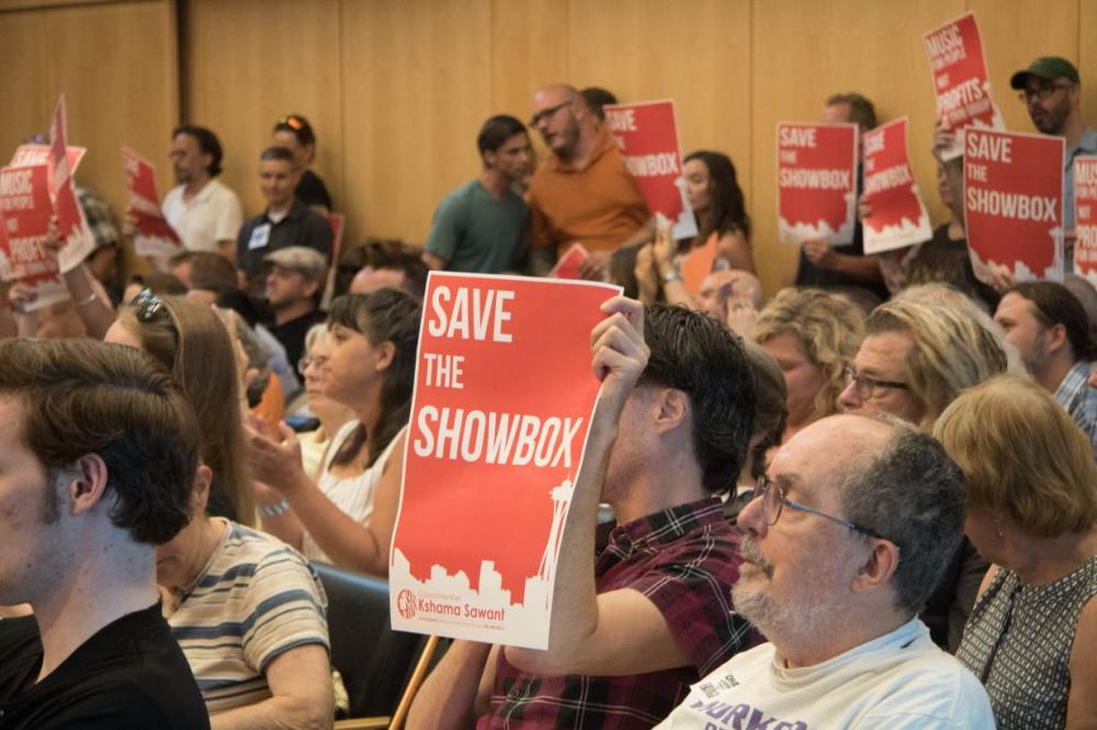 Supporters of music venue The Showbox wave signs at a Seattle City Council meeting. The venue now risks becoming the latest casualty of the Pacific Northwest city's real estate rush - and many in the community are saying enough is enough. - Thomson Reuters Foundation