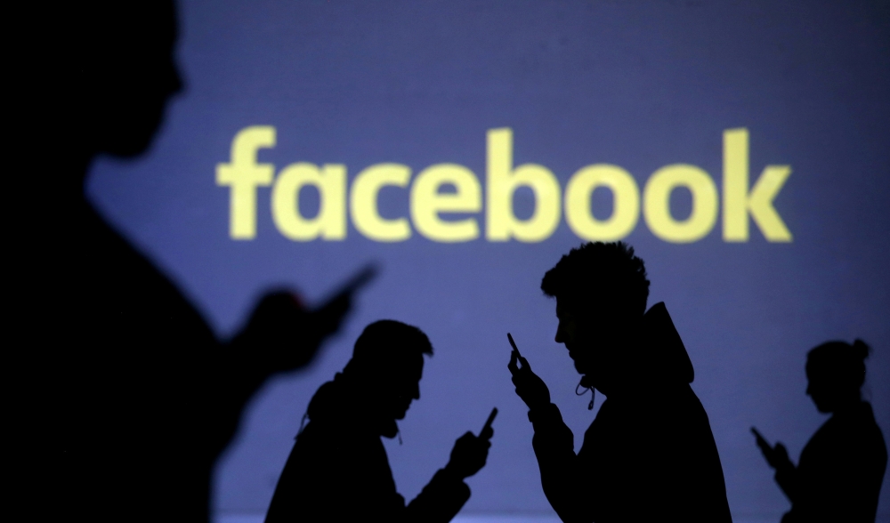Silhouettes of mobile users are seen next to a screen projection of Facebook logo in this picture illustration in this file photo. — Reuters