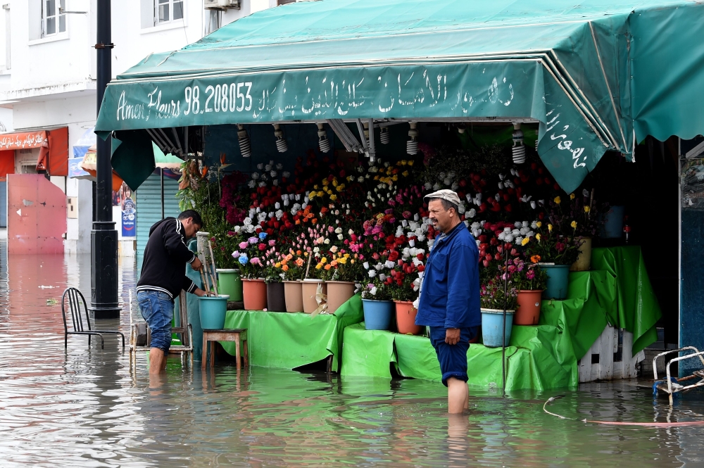 A shop owner tries to salvage his merchandise in a street flooded by torrential rains in the Tunisian capital Tunis on Thursday. — AFP