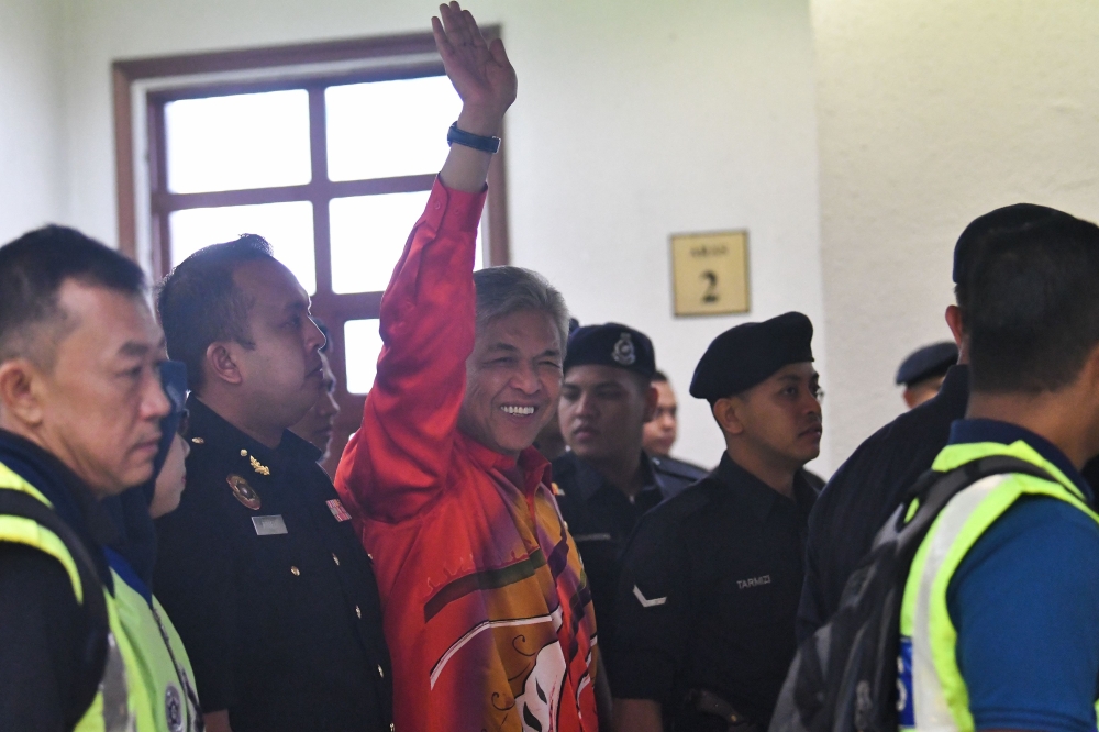 Detained Malaysia’s Deputy former Prime Minister Ahmad Zahid Hamidi escorted by police waves before entering a court in Kuala Lumpur to face charges on Friday. — AFP