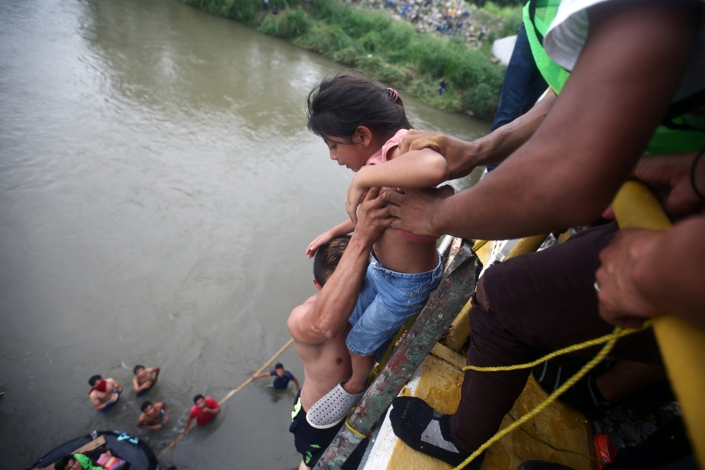 Central American migrant, part of a caravan trying to reach the US, holds a child as he goes down from a bridge that connects Mexico and Guatemala to avoid the border checkpoint in Ciudad Hidalgo, Mexico, Saturday. — Reuters