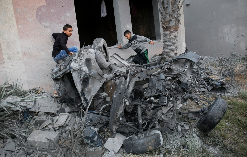 


Palestinians stand next to the remains of a car that was destroyed following an Israeli airstrike in Khan Yunis in the southern Gaza Strip, Monday.  — AFP