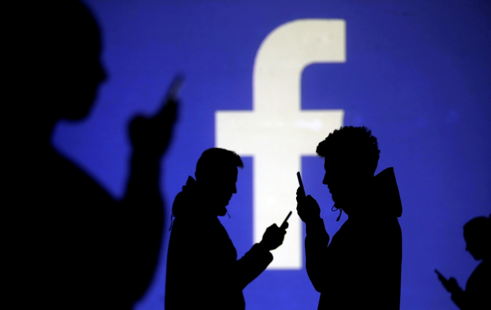 Silhouettes of mobile users are seen next to a screen projection of Facebook logo in this picture illustration taken on March 28, 2018.  — Reuters