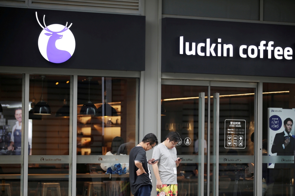 Men check their mobile phones outside a Luckin Coffee store in Beijing, China, in this file photo.— Reuters