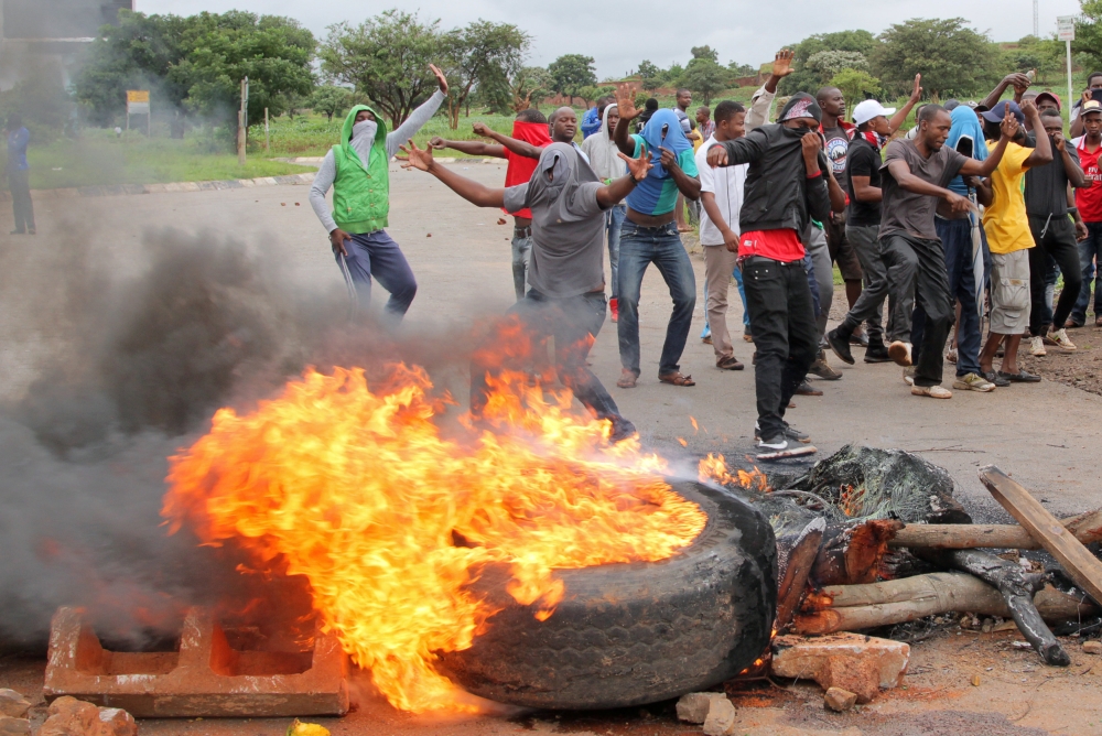 Protesters stand behind a burning barricade during protests on a road leading to Harare, Zimbabwe, on Tuesday. — Reuters