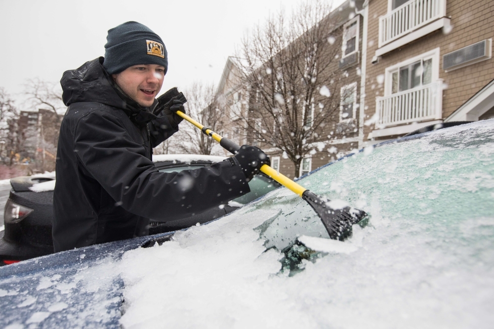 A man scrapes ice and snow off of his car following a winter storm that brought snow, rain, and a flash freeze in Quincy, Massachusetts, on Sunday. — AFP