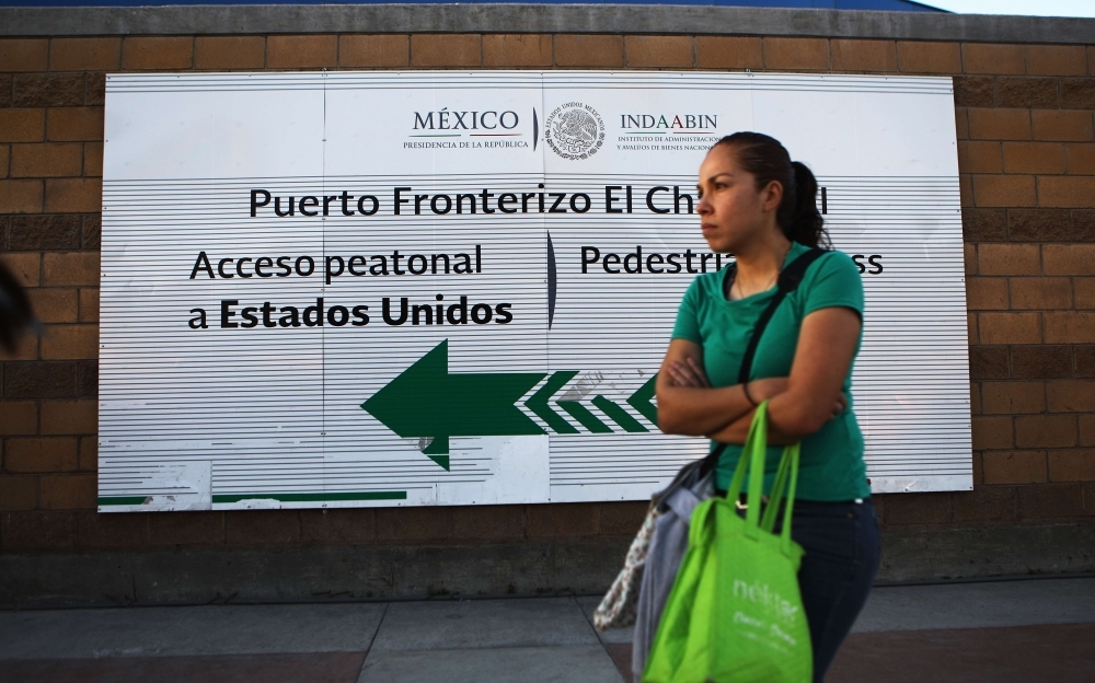 A woman stands at the El Chapparal port of entry, with a sign pointing toward the US, on Friday in Tijuana, Mexico. The Trump administration said it will begin forcing some asylum seekers currently in the US back across the border to Tijuana to wait in Mexico for their court cases to come up. — AFP