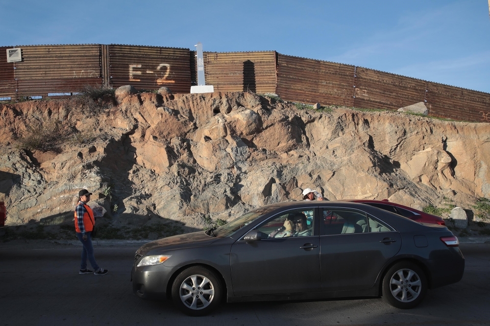 Motorists heading to the United States from Mexico wait along US border wall to pass through the port of entry on Sunday in Tecate, Mexico. — AFP