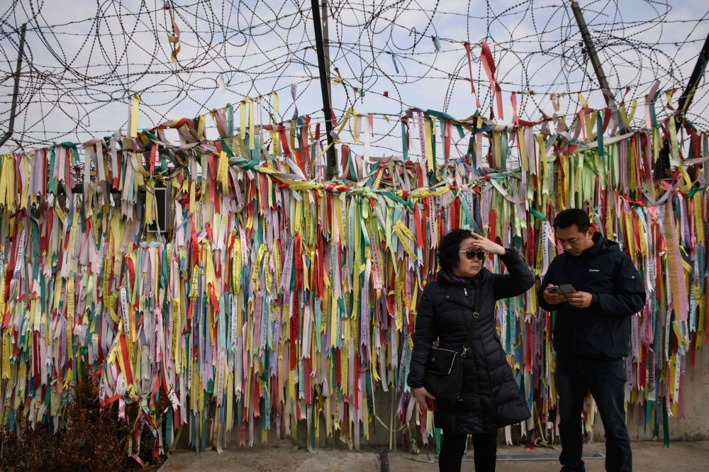 Visitors stand before a fence adorned with ribbons with messages written on them, at the Imjingak 'peace park' near the Demilitarized Zone (DMZ) separating North and South Korea, in Paju on Tuesday. — AFP