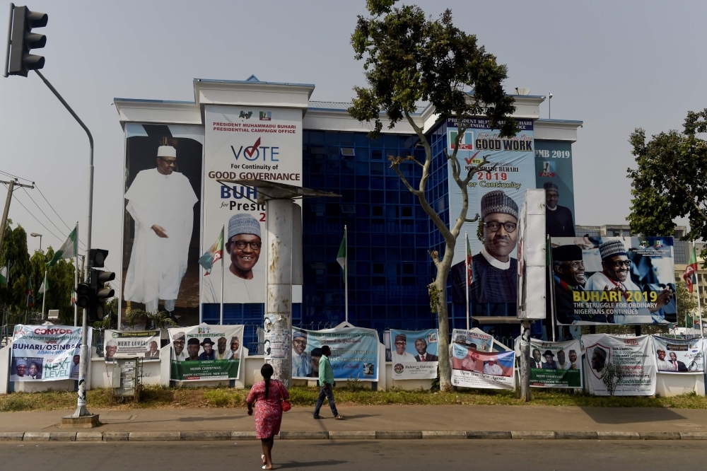 A woman walks to the campaign headquarters of the ruling All Progressives Congress (APC) party, displaying campaign posters of their candidate for re-election, President Mohammadu Buhari, in Abuja, on Saturday. Nigeria's president and ruling party were accused of dirty tricks to stifle opposition support, with one week to go before the election in Africa's most populous nation. — AFP