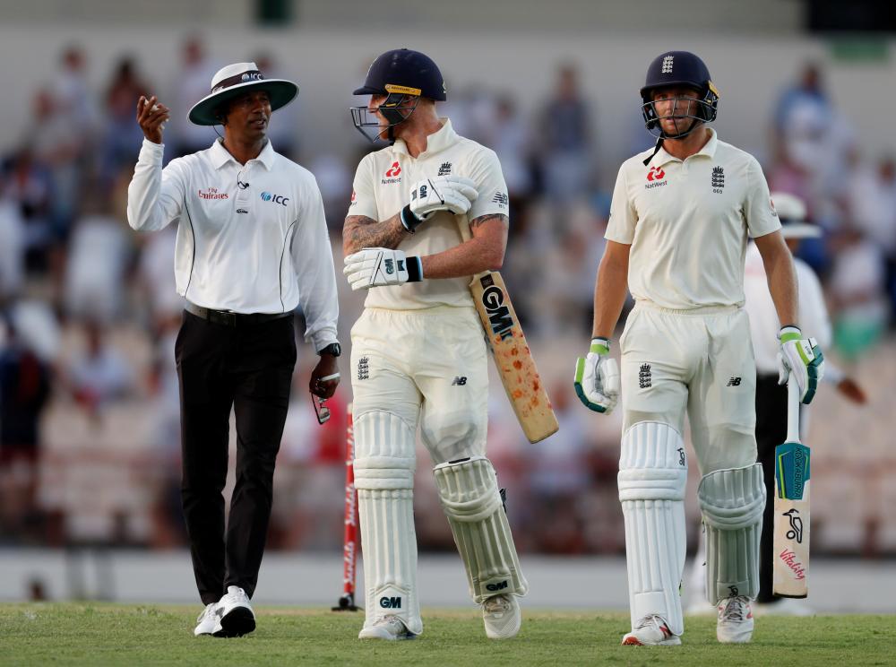 England’s Ben Stokes speaks with the umpire as Jos Buttler looks on while leaving the ground after first day’s play at Darren Sammy National Cricket Stadium in St Lucia Saturday. — Reuters