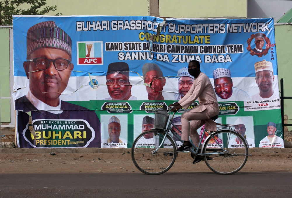 A cyclist drives pasts a campaign poster for President Muhammadu Buhari in a street after the postponement of the presidential election in Kano, Nigeria, on Sunday.  — Reuters