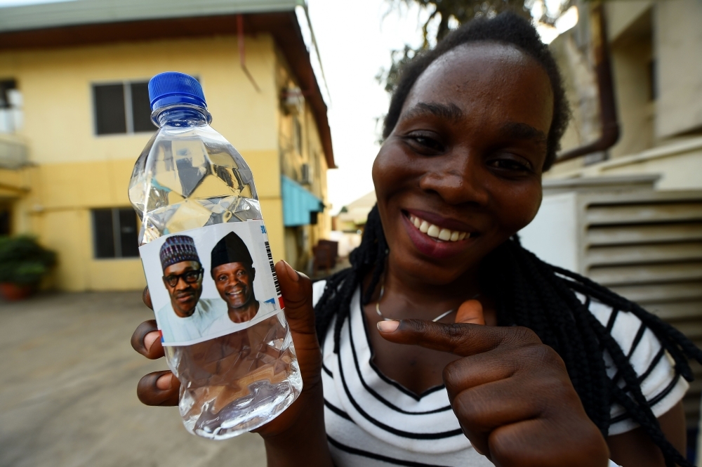 A woman holds a branded table water called Buhari Vendors and bearing photographs of candidates of the ruling All Progressives Congress (APC), Nigeria’s President Mohammadu Buhari and Vice President Yemi Osinbajo in Abuja, on Wednesday, ahead of rescheduled general elections. — AFP