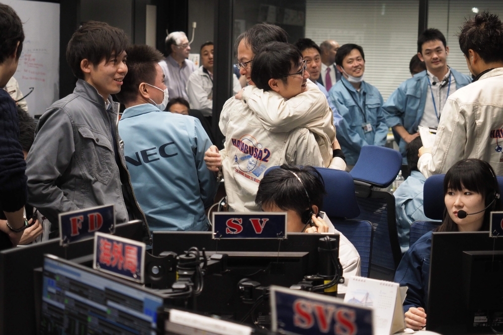  In this handout photograph taken and released by the Institute of Space and Astronautical Science (ISAS) of Japan Aerospace Exploration Agency (JAXA) on Friday, Yuichi Tsuda, center right, project engineer of the Hayabusa2 mission, hugs his colleague in the control room in Sagamihara, after the touchdown of the probe on the Ryugu asteroid. — AFP