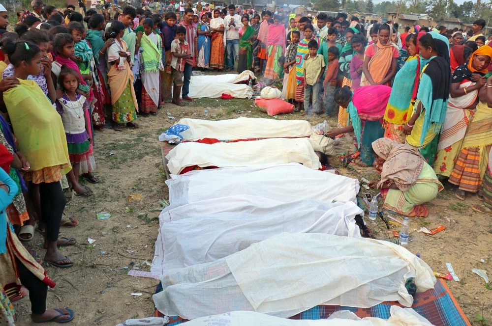 People stand next to the bodies of tea plantation workers, who died after consuming bootleg liquor, in Golaghat in the northeastern state of Assam, India, on Friday. — Reuters