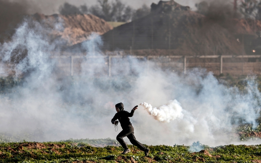 A Palestinian protester returns a tear gas canister thrown by Israeli troops during a demonstration near the fence along the border with Israel, east of Gaza City, on Friday. — AFP