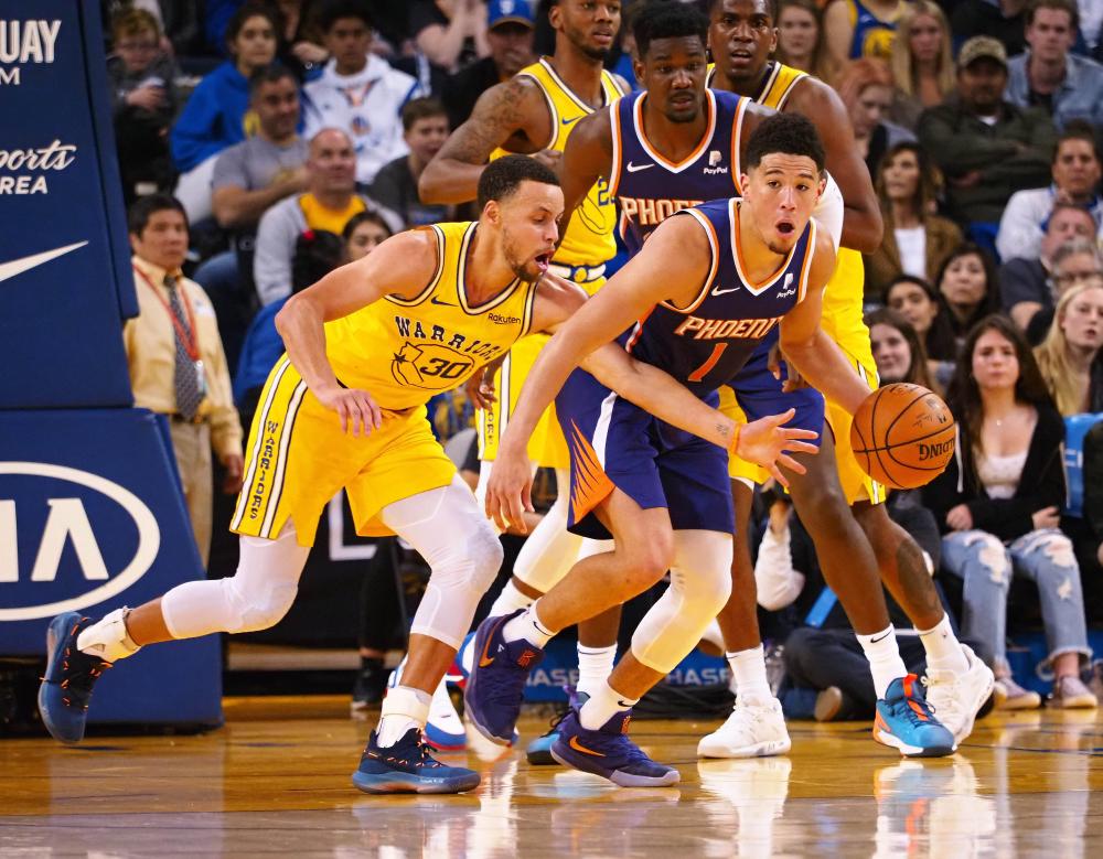 Phoenix Suns’ guard Devin Booker controls the ball against Golden State Warriors’ guard Stephen Curry during their NBA game at Oracle Arena in Oakland Sunday. — Reuters