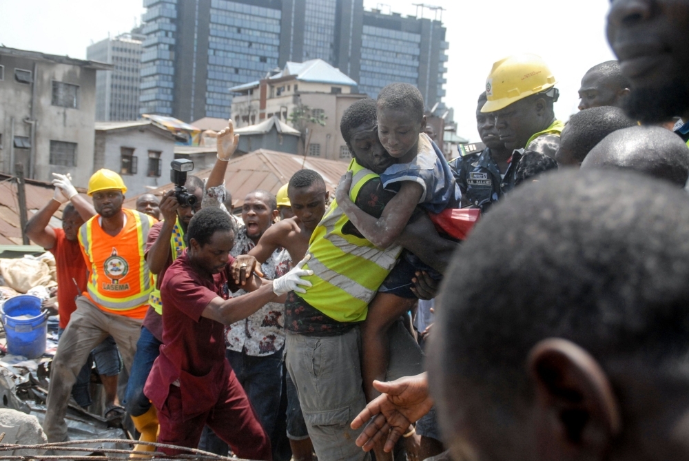 Emergency personnel rescue a child at the site of a building which collapsed in Lagos on Wednesday. At least 10 children were among scores of people missing after a four-story building collapsed in Lagos, with rescuers trying to reach them through the roof of the damaged structure. — AFP