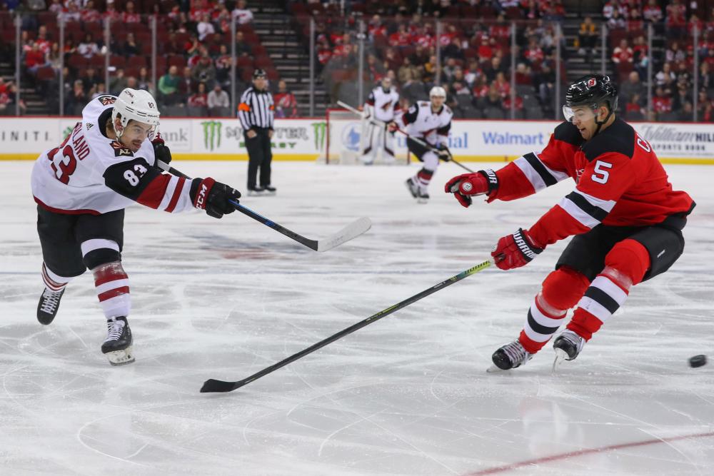 Arizona Coyotes’ right wing Conor Garland (L) shoots the puck past New Jersey Devils’ defenseman Connor Carrick during their NHL game at Prudential Center in Newark Saturday. — Reuters