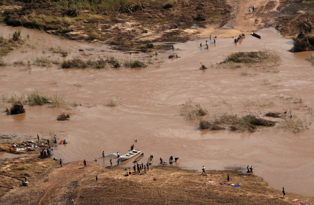 People stand on the banks where the bridge was washed away, in the aftermath of Cyclone Idai, near the village of John Segredo, Mozambique, on Sunday. — Reuters