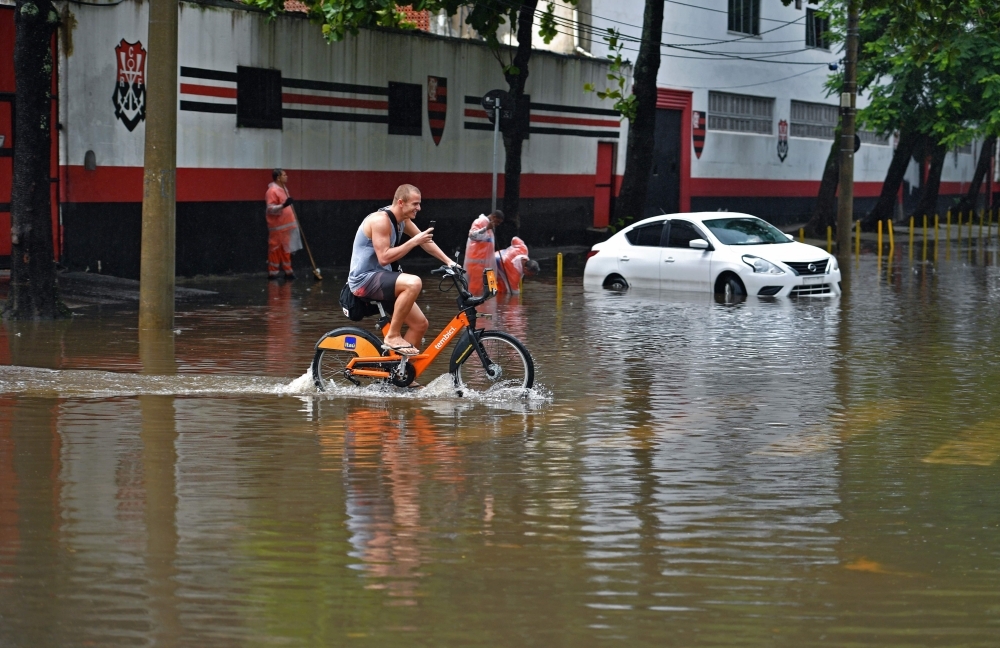 A cyclist makes a video of himself at a flooded area in Rio de Janeiro, Brazil, on Tuesday. — AFP