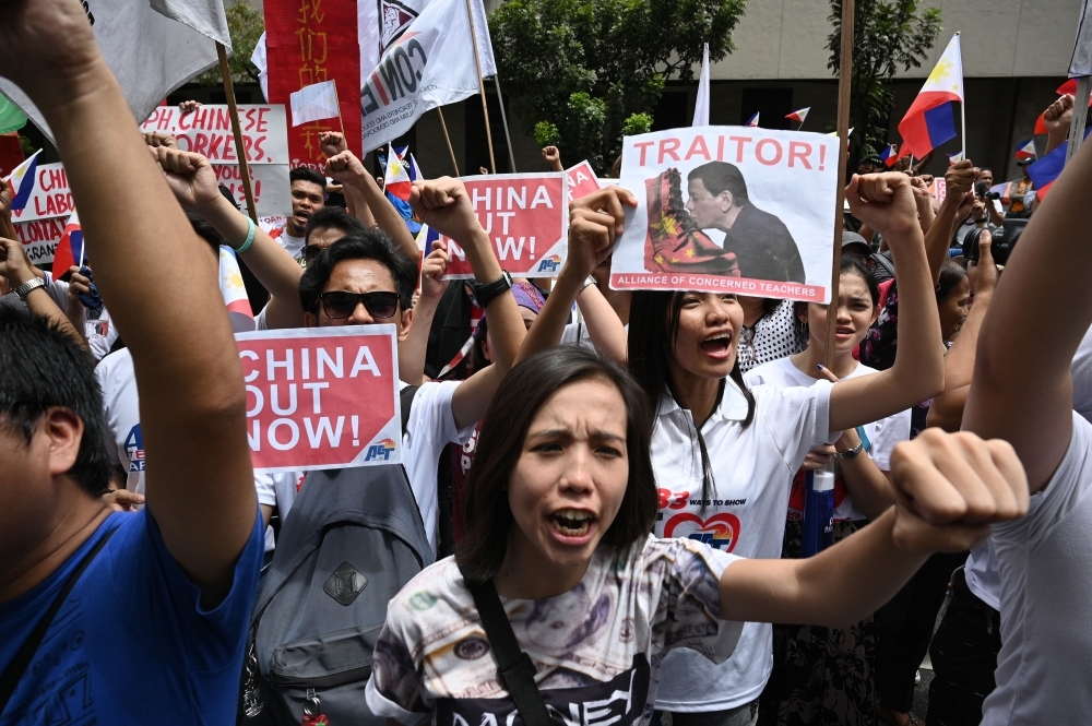 Anti-China protesters raise clinched fists and national flags as they shout slogans during a protest in front of the consular office of China, in the financial district of Manila, on Tuesday. — AFP