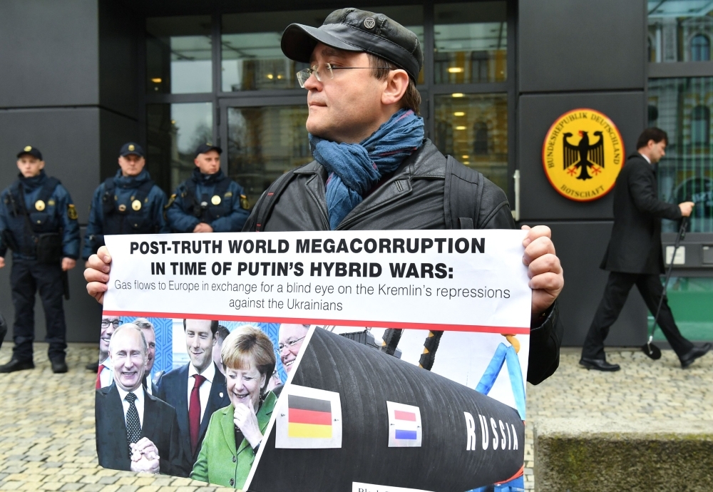 A man holds a placard depicting Russian President Vladimir Putin and German Chancellor Angela Merkel smiling, and the Nord Stream 2 gas pipe-line, during a rally in front of the German embassy in Kiev, on Thursday. Demonstrators held an action demanding to stop Germany's attempts to lift sanctions against Russia and to increase pressure to release detained Ukrainian. — AFP