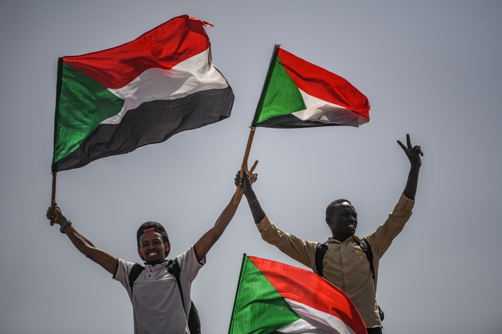 Sudanese protesters flash the victory sign and wave national flags during a rally outside the army headquarters in the capital Khartoum on Friday. — AFP