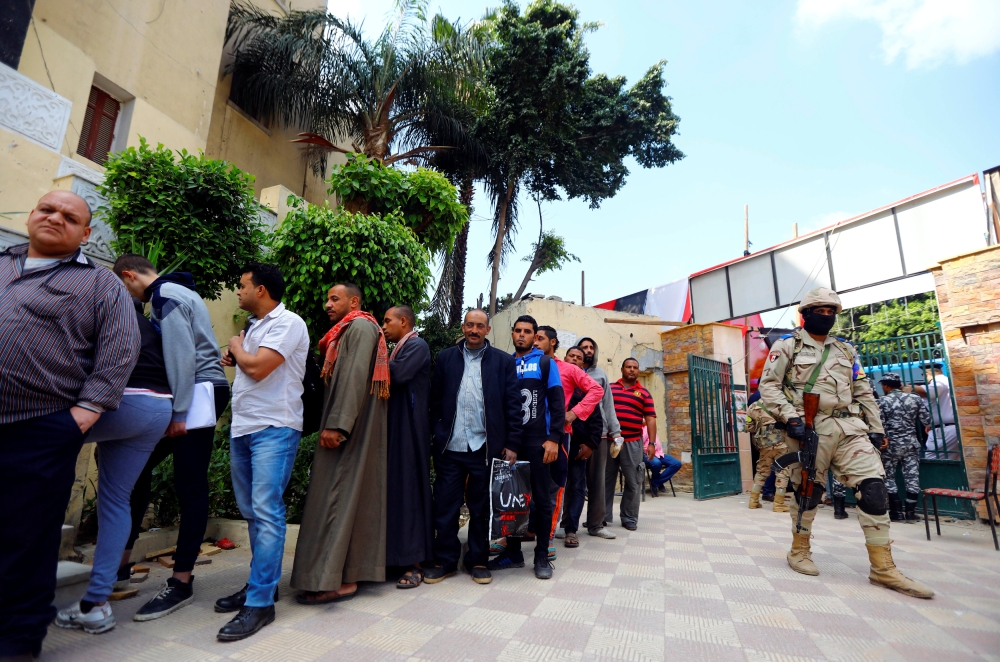 A soldier stands guard as people wait in line to cast their votes during the second day of the referendum on draft constitutional amendments, at a polling station in Cairo, Sunday. — Reuters