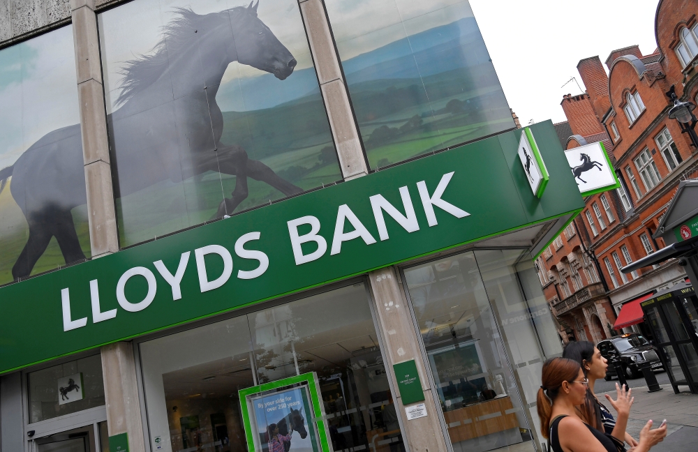 File photo shows a woman looks at her phone as she walks past a branch of Lloyds bank in London, Britain. — Reuters