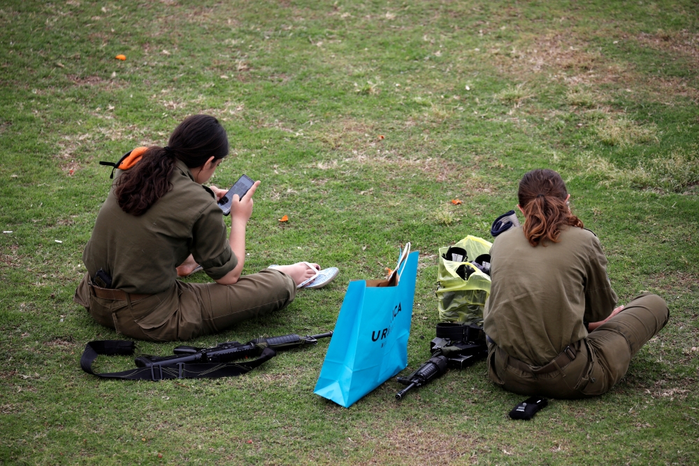 Female Israeli soldiers sit in a grassy area in the southern Israeli city of Ashkelon. — Reuters