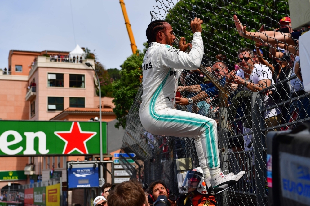 First placed Mercedes' British driver Lewis Hamilton, left, almost bends over after jumping at a fence to greet fans as he celebrates winning the pole position after the qualifying session at the Monaco street circuit on Saturday in Monaco, ahead of the Monaco Formula 1 Grand Prix. — AFP