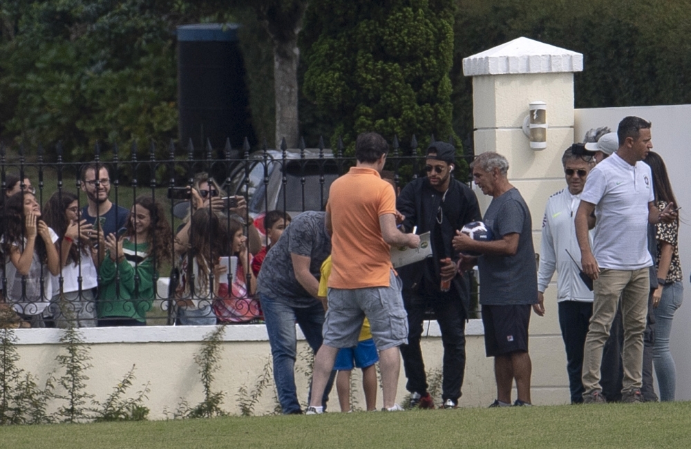 Brazil's footballer Neymar, in black wearing cap, signs an autograph upon arriving in helicopter at the Granja Comary sport complex in Teresopolis, Brazil, on Saturday. — AFP