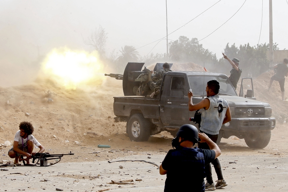 A fighter loyal to the Government of National Accord (GNA) fires a heavy machine gun as a press photographer take pictures of the scene during clashes against forces loyal to strongman Khalifa Haftar on Saturday in the Airport Road Area, south of the Libyan capital Tripoli. — AFP